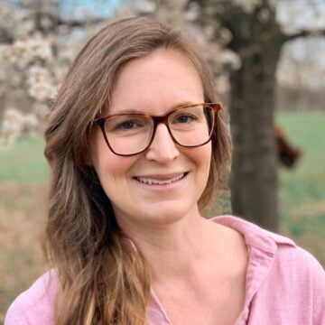 Headshot of woman in pink top wearing brown framed eyeglasses smiling directly at camera.