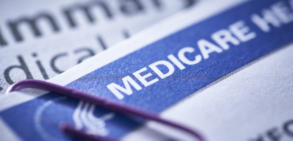 Medicare health insurance card up close with a purple paperclip on it with other papers behind it.