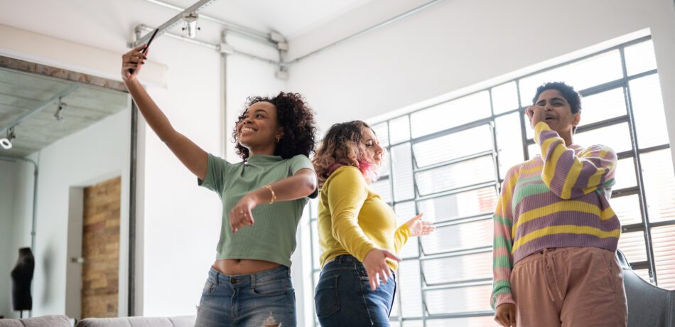 Young adults filming themselves with a smartphone while dancing and singing.