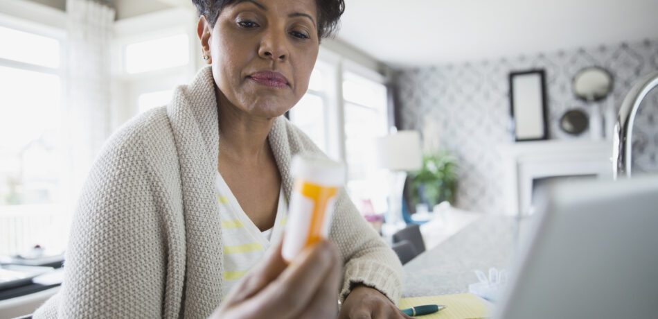 Woman reading prescription bottle label with her laptop in front of her.