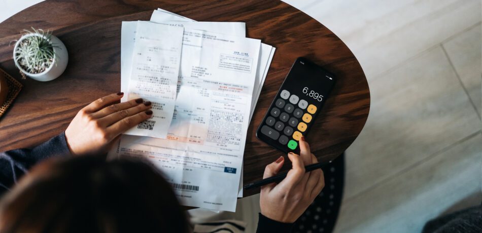 Overhead view of a woman looking at receipts and using a calculator.