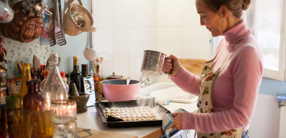 Woman in her kitchen sifting powdered sugar on a baking sheet of cookies.