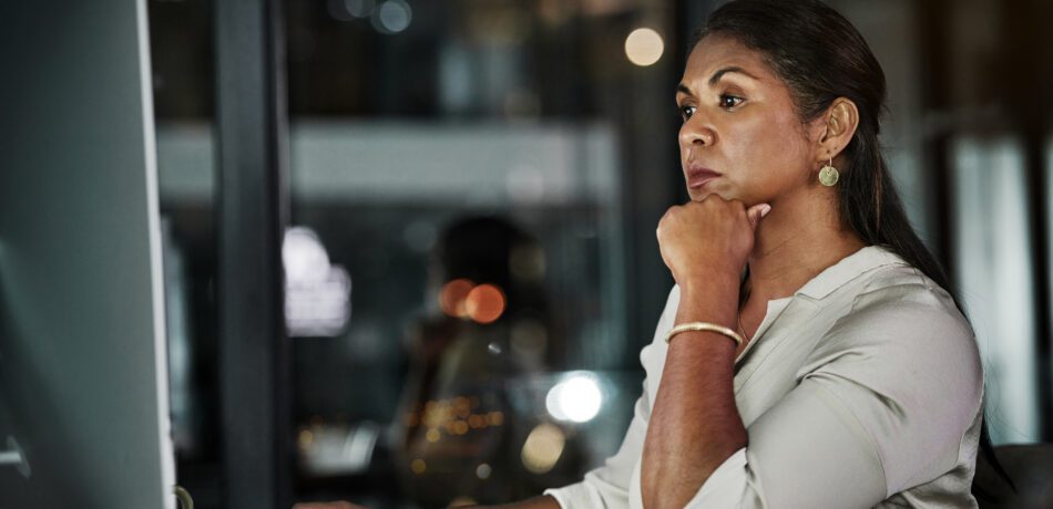 Mature looking woman working on a computer in an office at night.