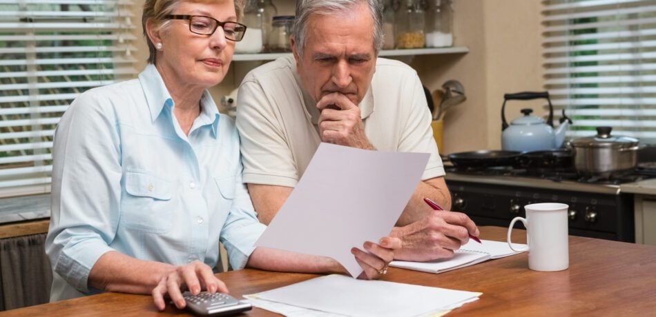 Senior couple sitting at their kitchen table looking at papers and taking notes over a cup of coffee.