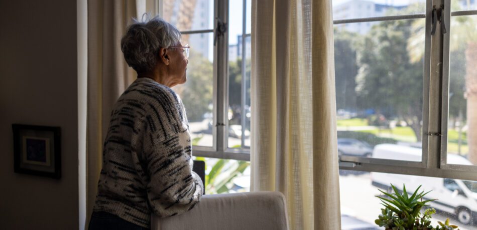 Senior woman looking out the windows of her home.