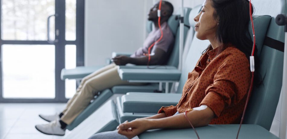 Man and woman donating blood in hospital sitting on recliners.