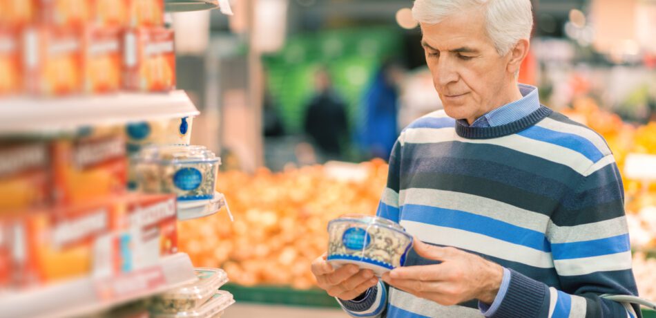 Senior man wearing a striped sweater reading the nutrition label on a food package.