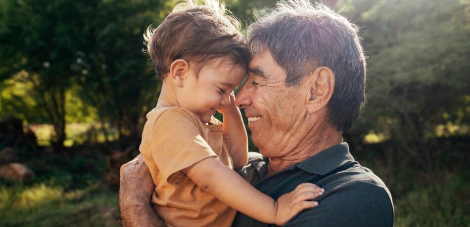 Grandfather holding his toddler grandson as they put their heads together smiling.