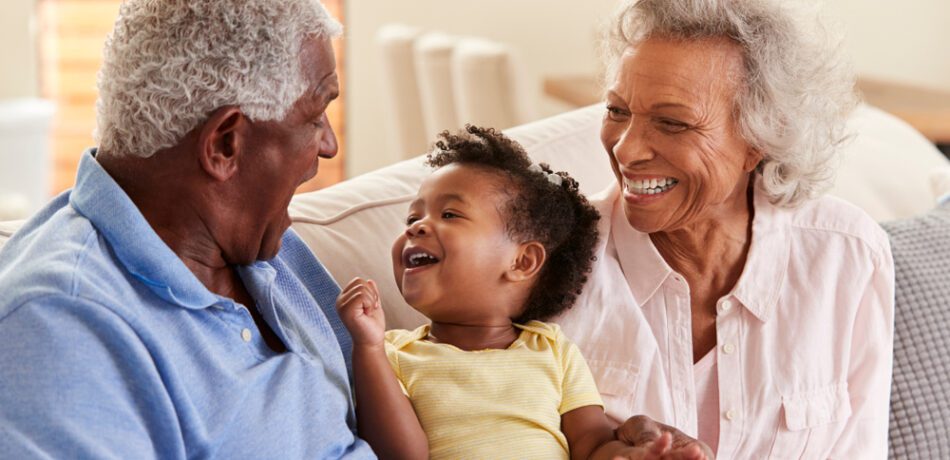 Older grandparents sitting on couch with young grandchild.