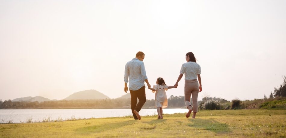 A family walks near a river while holding hands.