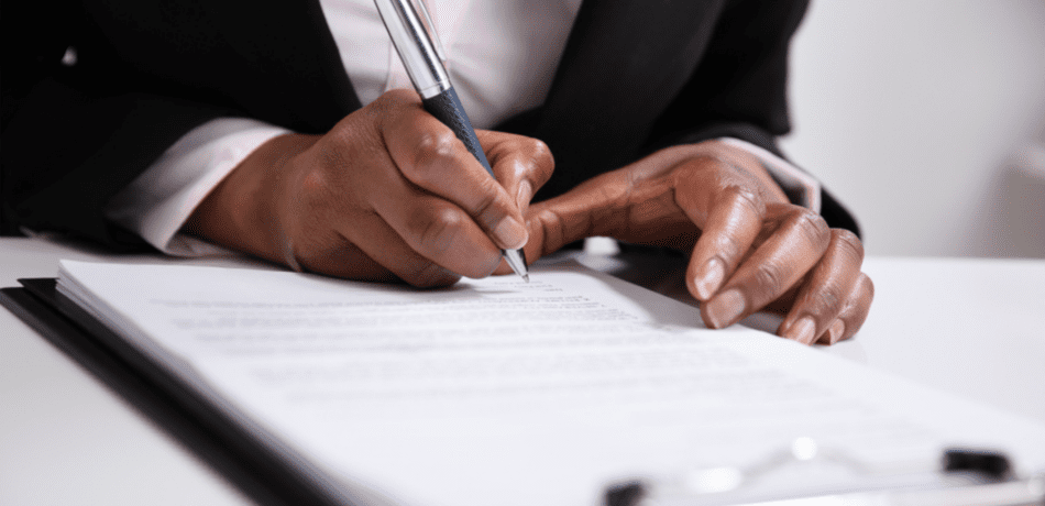 A woman's hands writing on a clipboard with a pen.