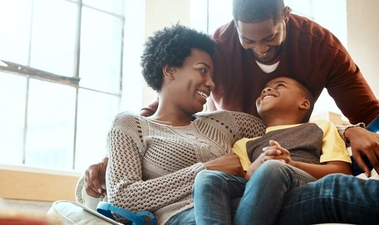 Younger couple holding their son on their lap on the couch while all smile.