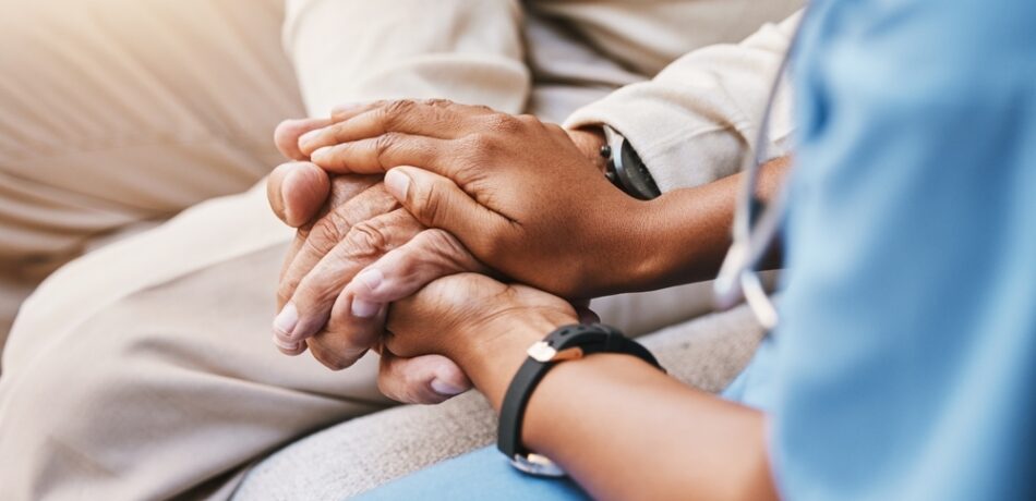 A medical professional holds hands with a patient, only their hands in their laps are visible.