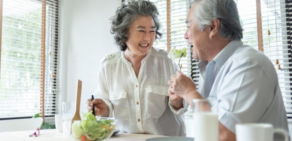 Older Asian couple smiling sitting in kitchen sharing a meal at the counter.