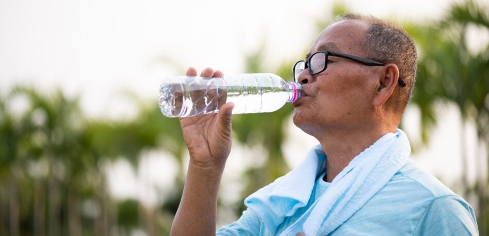Older Asian man is drinking water after exercising.