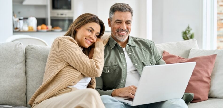 An older couple looks at a laptop while sitting on a couch.