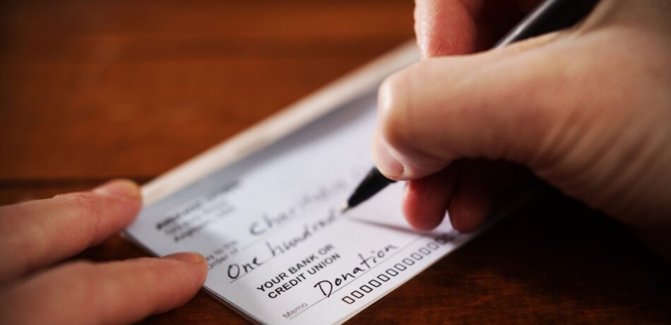 Close up of person's hand writing a donation check.