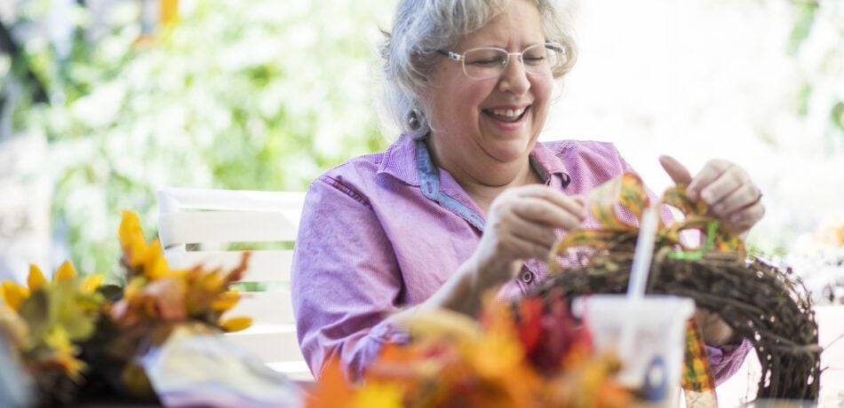 Senior woman making a fall wreath while smiling.