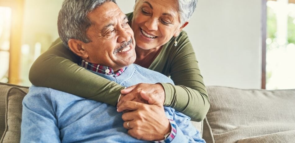 An older couple embraces on a couch.