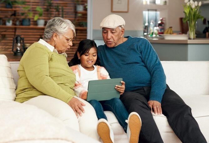 Grandparents sit on a couch with their granddaughter.