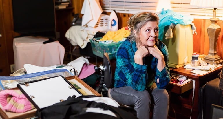 A woman sits in a cluttered room.