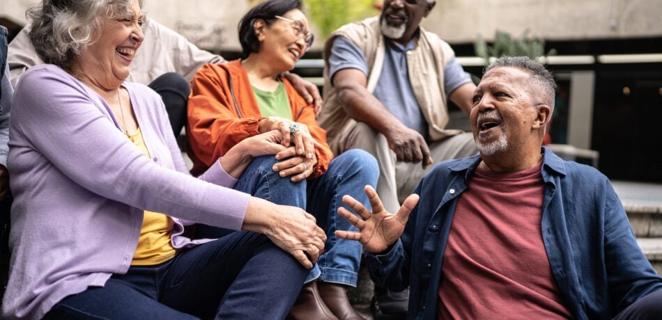 Senior friends sitting on steps laughing and talking outdoors.