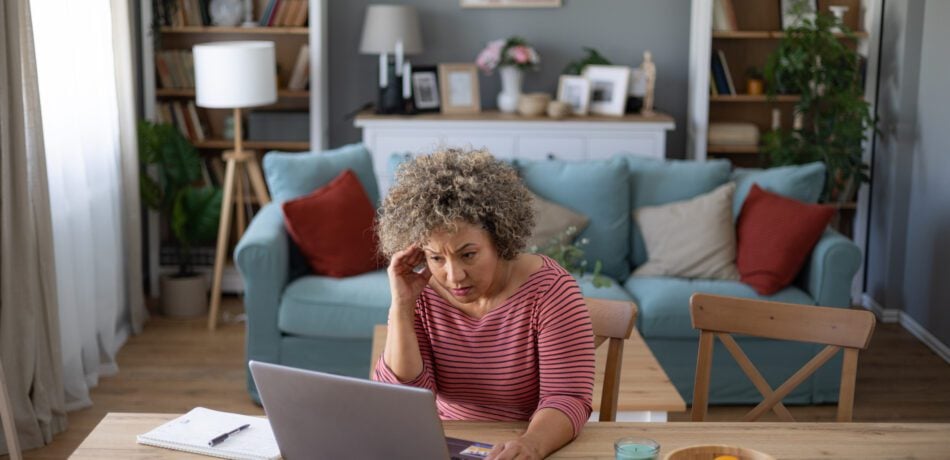 Concerned older woman looking at her open laptop on her desk.