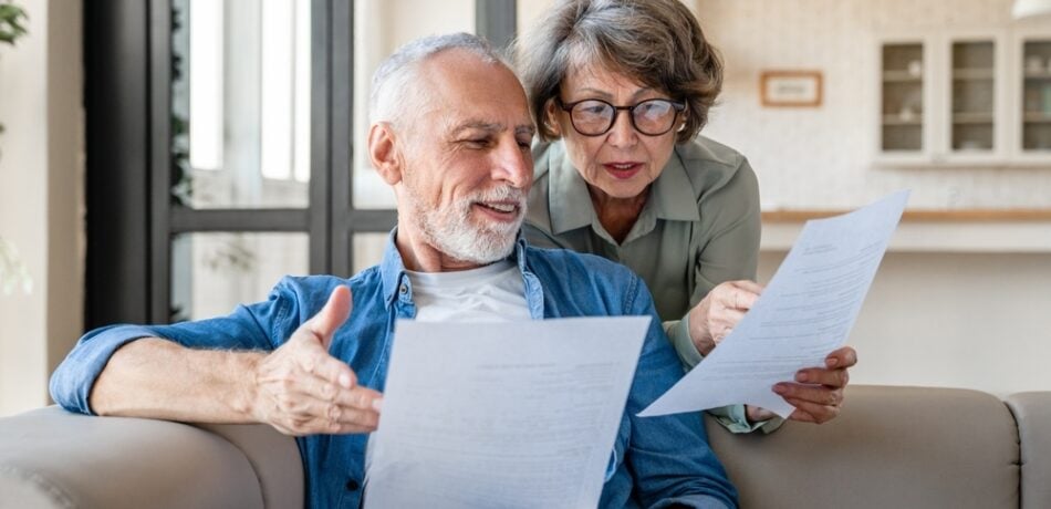 An older couple reads financial documents in their living room.