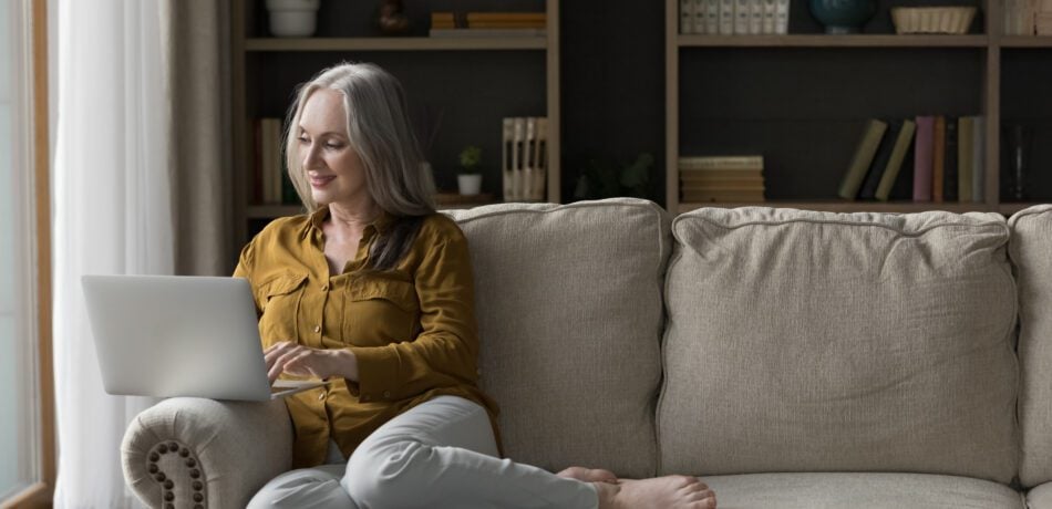 Older woman sitting on a couch using a laptop.