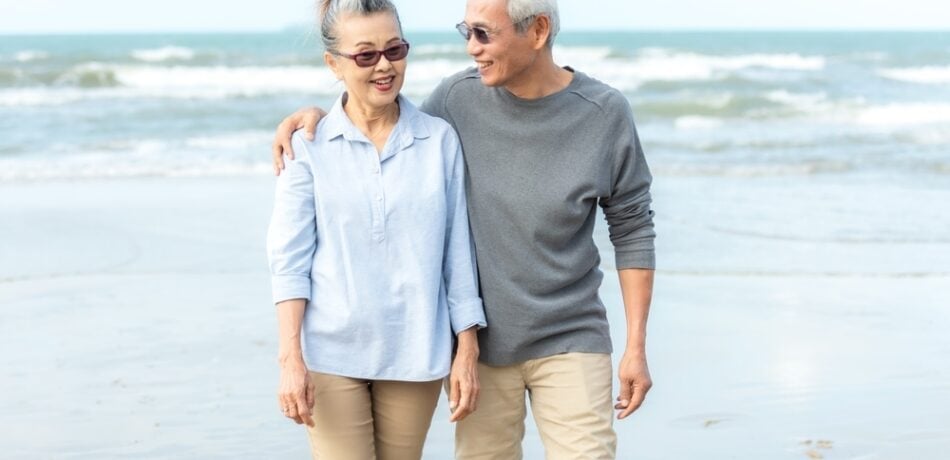 A senior couple walks on the beach.