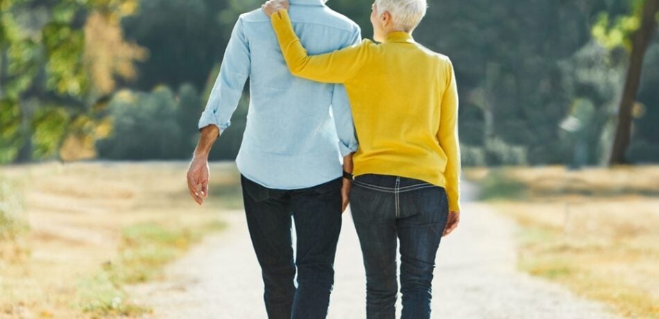 Senior couple walks outdoors while holding hands.