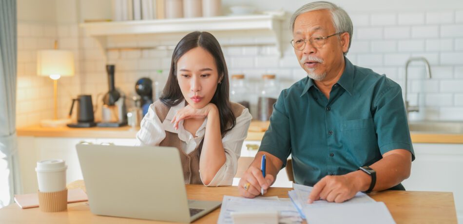 An adult daughter and elderly father review finances and estate planning matters in their home.